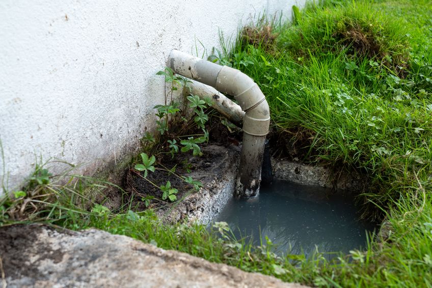 Pipe is leaking water into a grassy area. the grass is wet and the ground is muddy